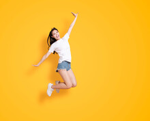 Happy Young Woman Jumping And Looking At The Camera Over Yellow Background