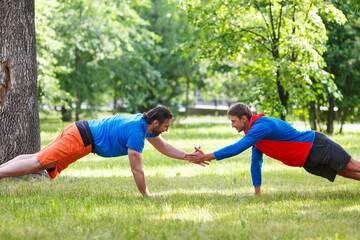 Two men doing push-up in public park ang giving five.