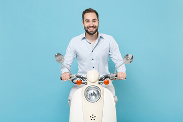 Wall Mural - Smiling young bearded man guy in casual light shirt driving moped isolated on pastel blue wall background studio portrait. Driving motorbike transportation concept. Mock up copy space. Looking camera.