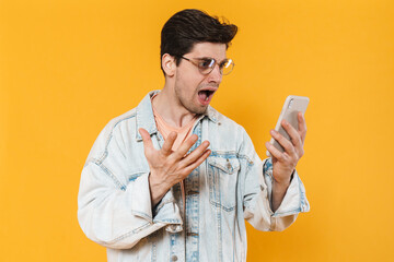 Poster - Photo of shocked young man in eyeglasses screaming and using mobile