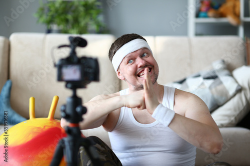 Young man in sport headband hitting hand with fist and looking at camera with funny expression