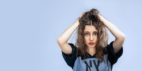 one slim brunette girl with long hair in a T-shirt with short shorts. girl covered her ears with her hands. sad girl hold face on blue background