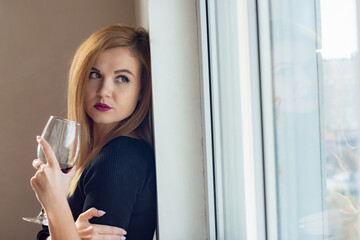 portrait of a girl looking sadly out the window with wine in her hands