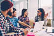 © BullRun - Hipster students in casual wear communicating with each other and discussing plan of collaboration sitting at meeting table with laptop computer in office.Team of young people cooperating on task