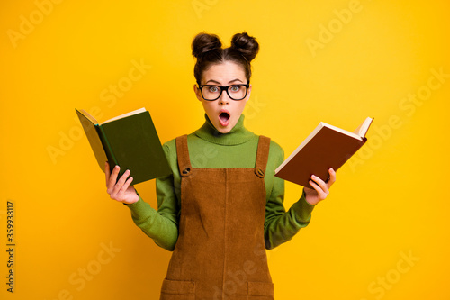 Portrait of her she nice attractive stunned wondered knowledgeable girl nerd reading two book compare preparing test isolated bright vivid shine vibrant yellow color background