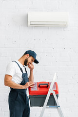 Wall Mural - Injured workman with finger near mouth opening toolbox on ladder near air conditioner on wall