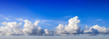 White Fluffy Yet Majestic Cumulus Clouds On Deep Blue Sky Background, Panoramic Format