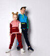© FAB.1 - Kids, boy and girl, in colorful tracksuits, sneakers. They smiling, posing isolated on white studio background. Hands in pockets