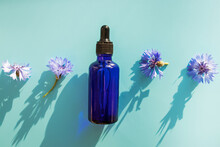 Cosmetic Oil Or Serum, Bluet Bottle And Flowers On Blue Background