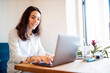 © Westend61 - Portrait of smiling young woman working on laptop at home office