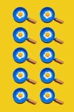 Pattern Of Rows Of Fried Eggs On Blue Pans Against Yellow Background
