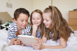 © Westend61 - Portrait of boy and his two sisters lying on bed using digital tablet for homeschooling