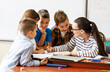 © BalanceFormCreative - Female teacher helps school kids to finish they lesson.They sitting all together at one desk.