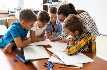 Wall Mural - Female teacher helps school kids to finish they lesson.They sitting all together at one desk.