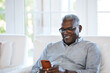 © Trinette Reed/Stocksy - African American Senior man texting on a smart phone sitting on the sofa at home