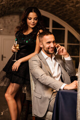 Wall Mural - Romance and dating concept. Young couple man and woman with champagne glasses celebrating and toasting in restaurant. Two people male and female in elegant evening suit and dress on romantic dinner