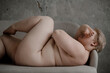 © Alina Hvostikova/Stocksy - Naked woman with overweight lying, hiding face.