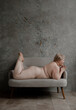 © Alina Hvostikova/Stocksy - Naked woman with overweight lying on stomach on sofa.