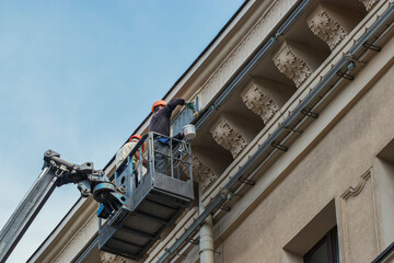 Reconstruction of the building of the Drama Theater in the city. Two working painters on an air platform paint a wall.