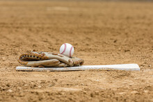 Baseball Glove And Ball Sitting On Pitching Mound Rubber On Infield Of Baseball Field. Concept Of Youth And School Sports, Summer Recreation And Outdoor Activity