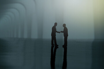 Silhouette of two businessmen make an handshake partnership agreement. Miniature people figure conceptual photography