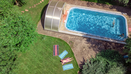 Wall Mural - Happy family relaxing by swimming pool, aerial drone view from above of parents and kids have fun on vacation, family weekend on resort
