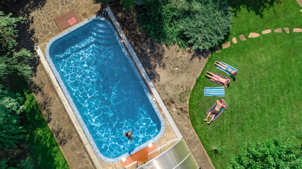 Wall Mural - Happy family relaxing by swimming pool, aerial drone view from above of parents and kids have fun on vacation, family weekend on resort
