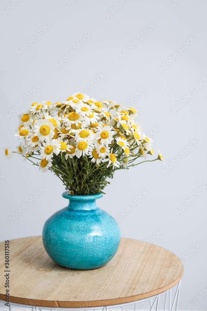 Vase with beautiful chamomiles on table against light background