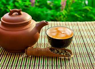 Wall Mural - Chinese tea cerermony in the garden. Clay teapot with ceramic cup, dry green tea in wooden scoop on a bamboo table.