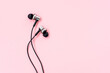 A pair of black music earphones for smartphone on a pastel pink background. Minimalist flat lay. Place for writing. Copy space.