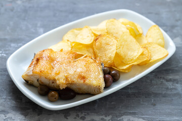 Sticker - fried cod fish with olives and potato chips on white dish on ceramic background