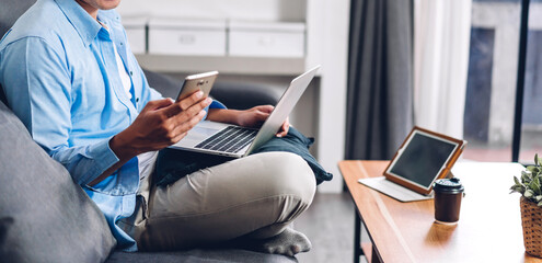 Young smiling asian man relaxing using laptop computer working and video conference meeting at home.Young creative man looking at screen typing message with smartphone.work from home concept
