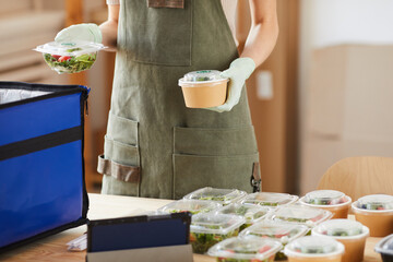 Close-up of young woman packing the boxes with fresh vegetables in bag she working in delivery service