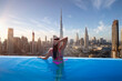 Beautiful young woman enjoys the panoramic view from an infinity pool on downtown Dubai