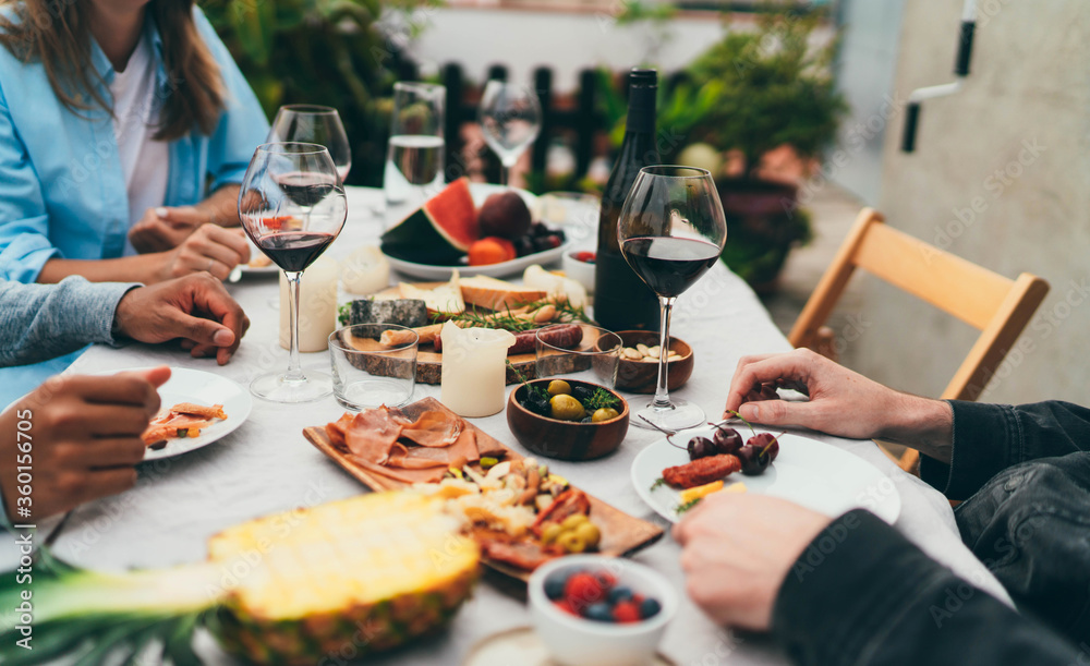 Group of young people dressed in casual clothes dining together drinking red wine and eating snacks, fruits, Friends celebrating birthday sitting in restaurant with small garden enjoying atmosphere - obrazy, fototapety, plakaty 