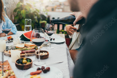 Multi cultural group of people dining together outdoors, Man pouring red wine into glass during cozy family dinner with festive table served with mediterranean food, Friendship Dinner Hanging Out