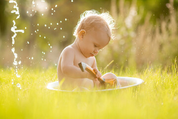 Cute little girl sits in a basin of summer water on the green grass