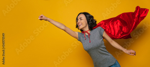 Fotomural To new adventures! A young, beautiful girl, pretending she is a superwoman, and flying in a classic superman pose, but with superman red cloak, that is flattering on the wind
