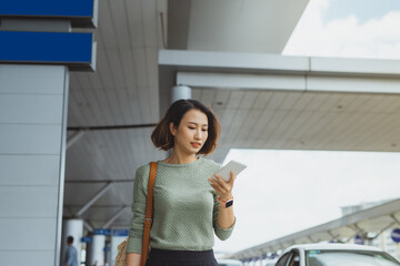 Wall Mural - Young businesswoman using phone to check her flight when standing outside.