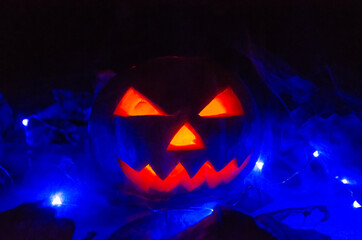 Wall Mural - Orange pumpkin with glowing eyes, mouth in the dark in blue lighting in the smoke close-up. concept of Halloween.