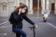 © wavebreak3 - Caucasian woman wearing a protective mask on her bike, wearing earphones in the streets