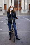 Fototapeta Miasto - Caucasian woman wearing a protective mask on her bike, wearing earphones in the streets