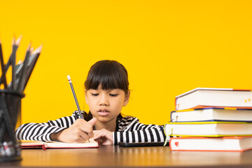 Young Asian kid, Thai girl writing and note on table with yellow background