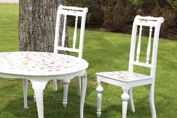 Idyllic seating in the garden. White wooden furniture on green lawn. Two folding chairs and white table in front of a green hedge.