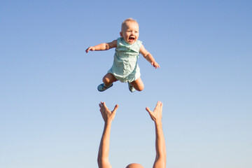 Man throws baby up against the blue sky. Concept game with children, happy family