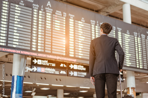 Fotomural Businessman standing at time flight schedule billboard hold the smartphone at airport terminal gate
