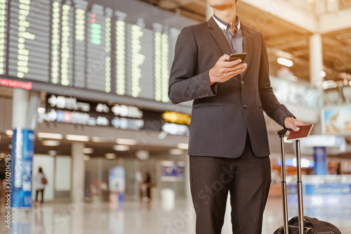 Cuadros en Lienzo Businessman standing at time flight schedule billboard hold the smartphone at airport terminal gate