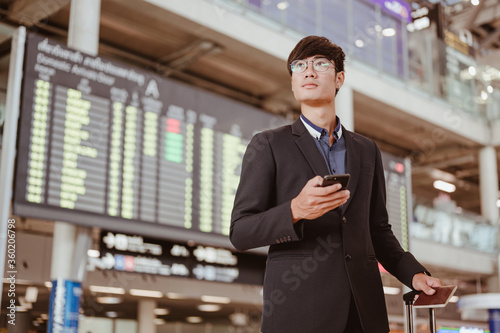 Cuadros en Lienzo Businessman standing at time flight schedule billboard hold the smartphone at airport terminal gate