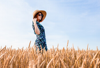 Stylish girl in a hat and glasses on a background of a wheat field