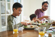 © trevor adeline/Caia Image - Smiling boy eating dinner with family at table